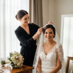 Nevěsta s krajkovým závojem a stylistkou v elegantní pracovně před svatbou.