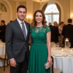 Muž a žena ve formálním oblečení stojí v elegantní banketní síni s hosty a stolky v pozadí